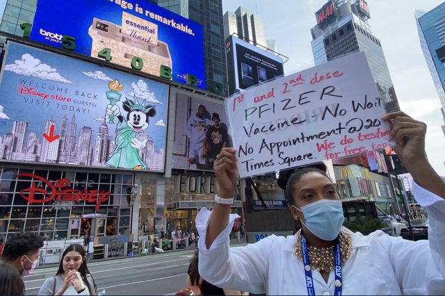 Tanika Price, a nurse who has been hailed as NYC's first vaccine hawker, holds up a sign for walk-in vaccine appointments near the Disney Store in Times Square while passerbys walk by.